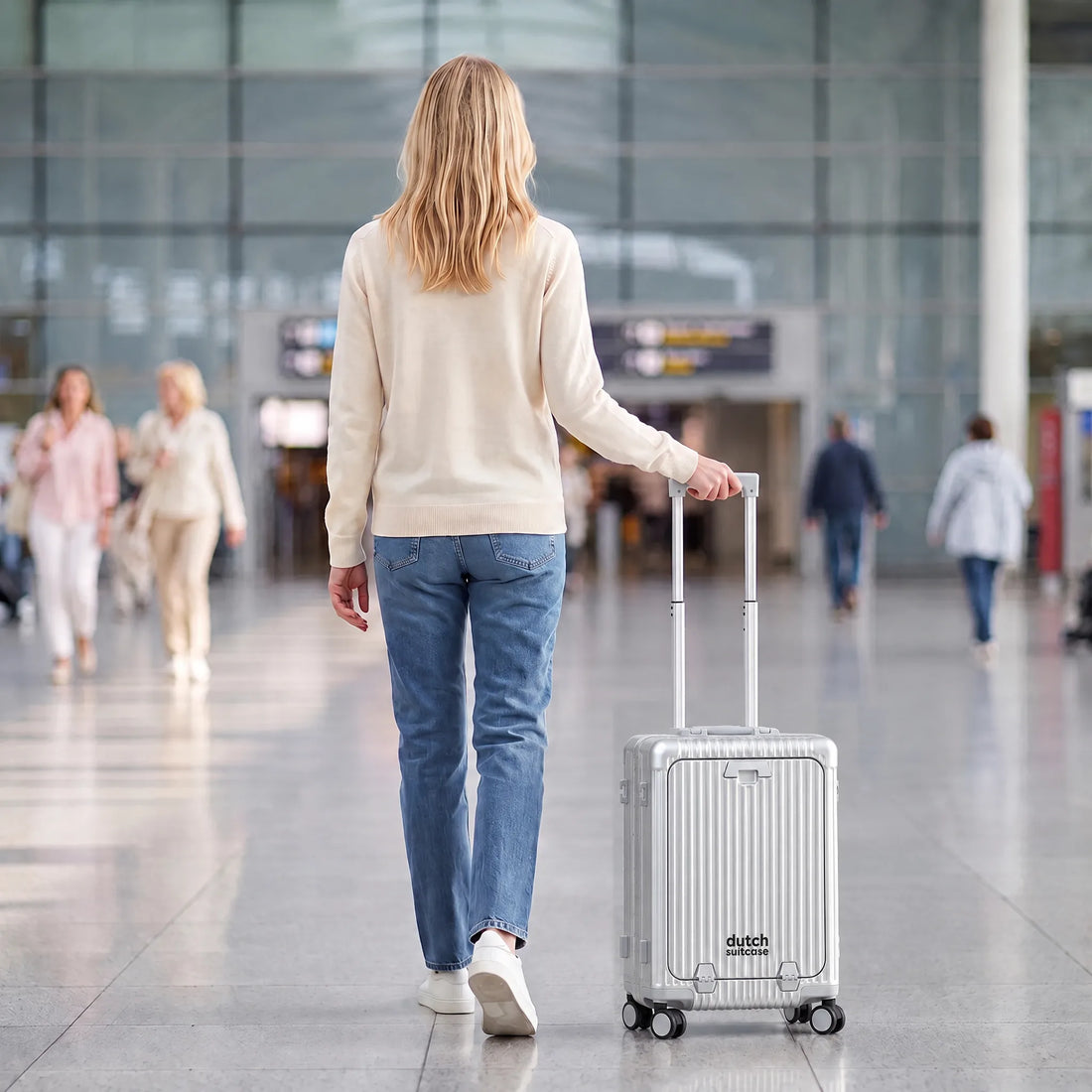 Vrouw loopt met de zilveren DS Front handbagage koffer aan de trolleystang door een luchthaventerminal