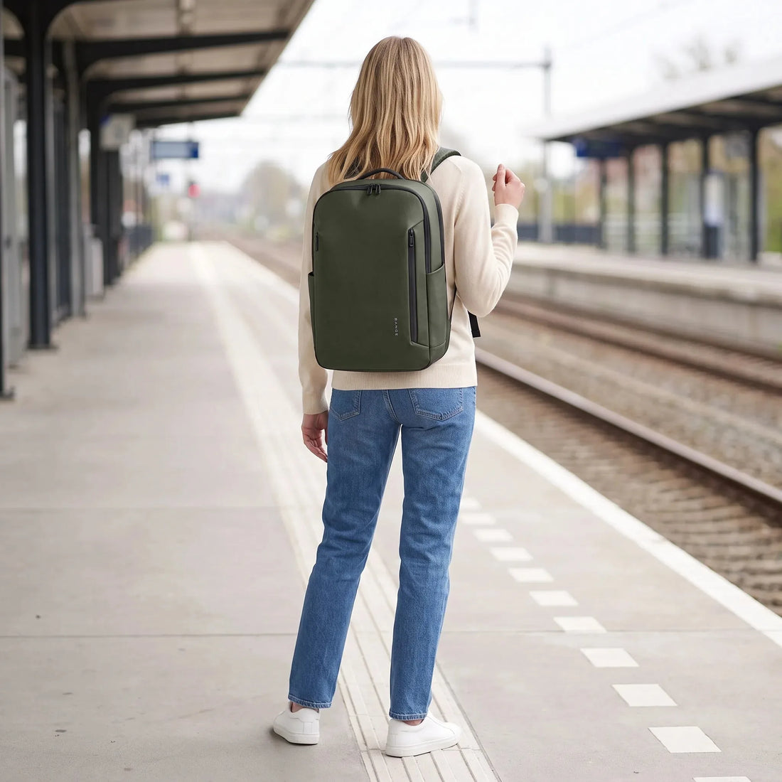Vrouw draagt de donkergroene DS Shield laptoprugzak op een treinperron, klaar voor vertrek