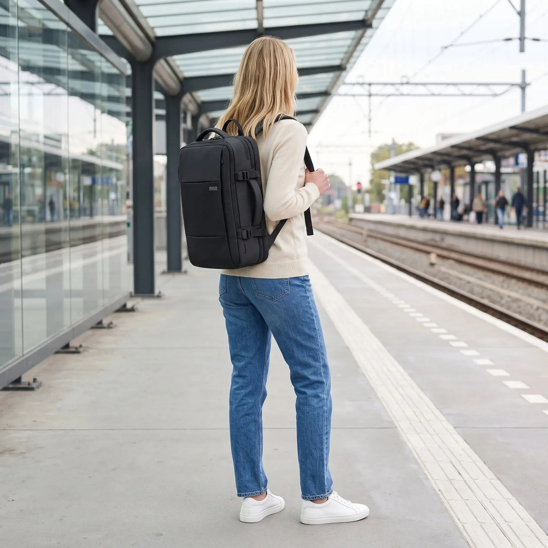 Vrouw draagt de DS Explorer reisrugzak van Dutchsuitcase op een treinperron, klaar voor vertrek