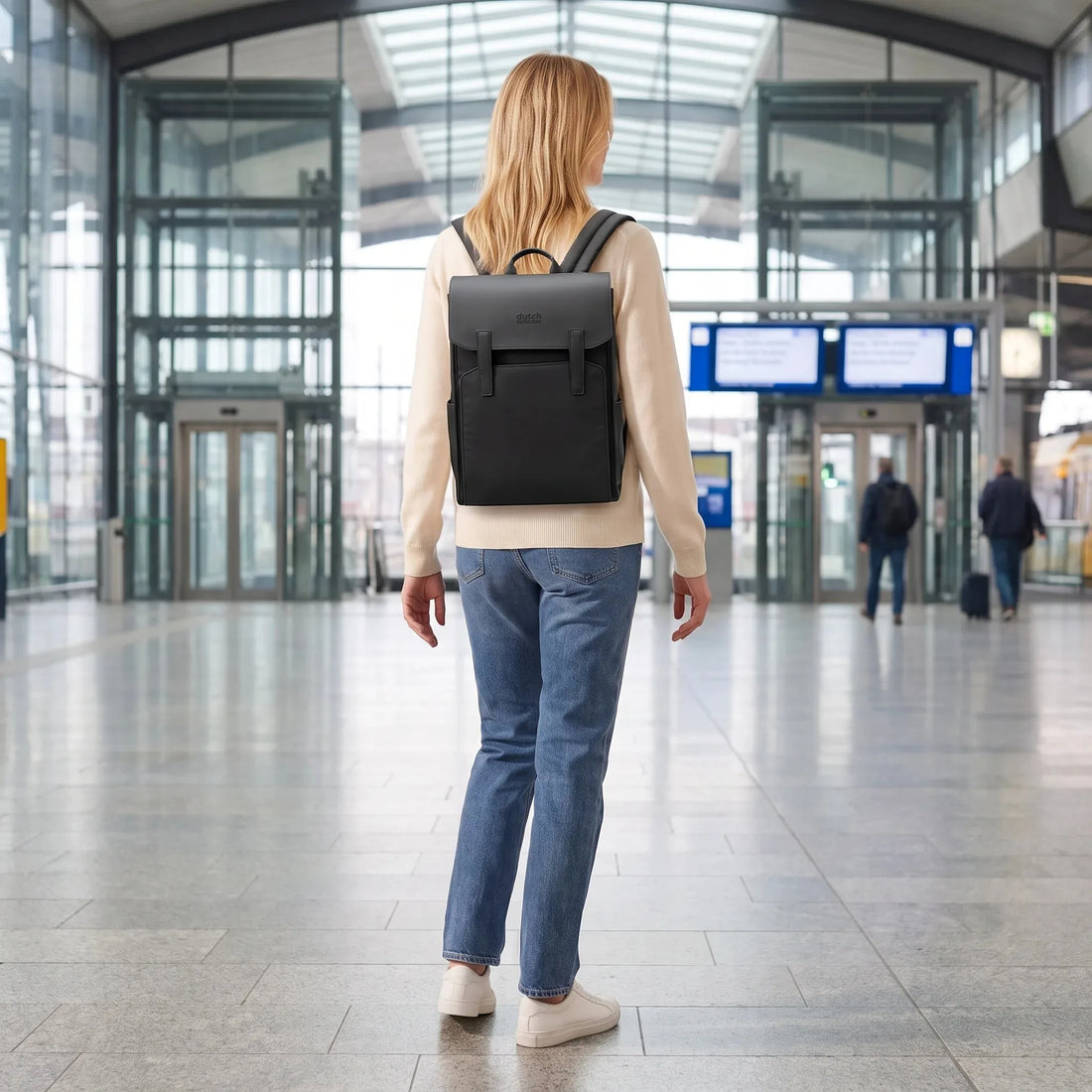 Vrouw draagt de zwarte DS Classic laptop rugzak van Dutchsuitcase in een stationshal tijdens het reizen