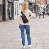 Vrouw draagt de zwarte DS Lock crossbody tas op de rug in een drukke winkelstraat, veilig op reis