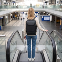 Vrouw draagt de zwarte DS Pro laptop rugzak op de roltrap in een stationshal
