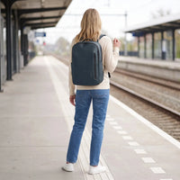 Vrouw draagt de donkerblauwe DS Shield laptoprugzak op een treinperron, klaar voor vertrek