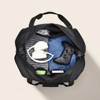Geopende DS Dark reistas gevuld met kleding, koptelefoon en powerbank toont het ruime hoofdvak
