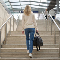 Vrouw loopt met de zwarte DS Dark reistas een stationstrap op, weekendtas voor onderweg